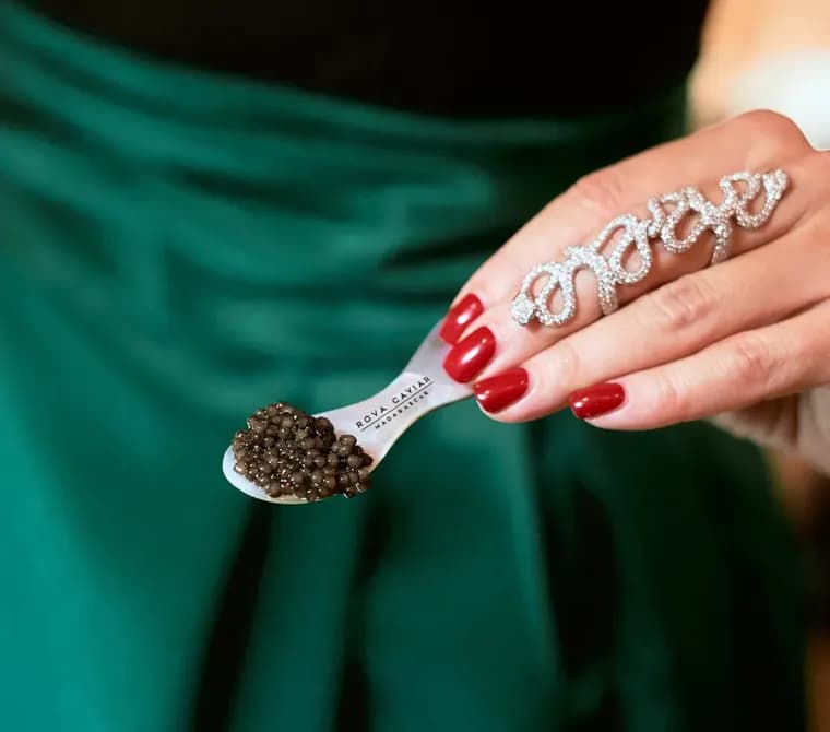 Cuillère en nacre garnie de caviar tenue au-dessus d'une robe de soirée verte